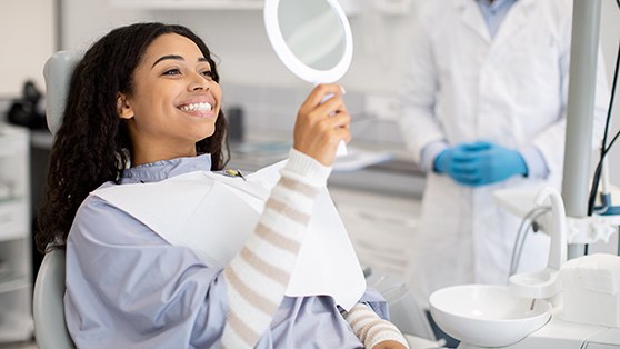 Woman smiling at reflection in handheld mirror