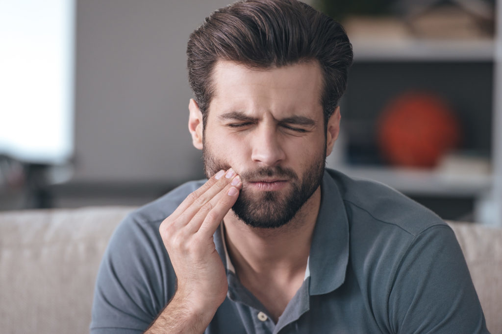 man holding his mouth because of tooth pain